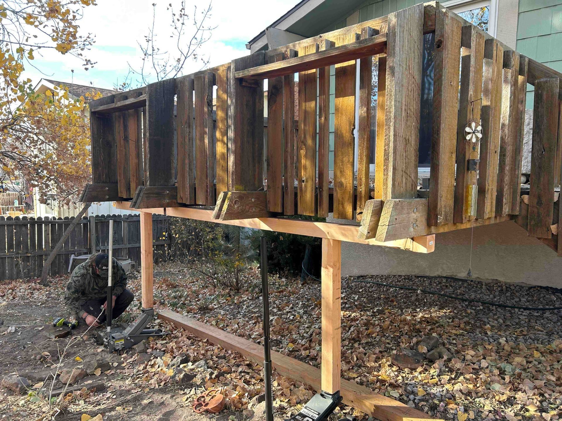 Wooden deck built of reclaimed wood, supported by new lumber; person works at base.