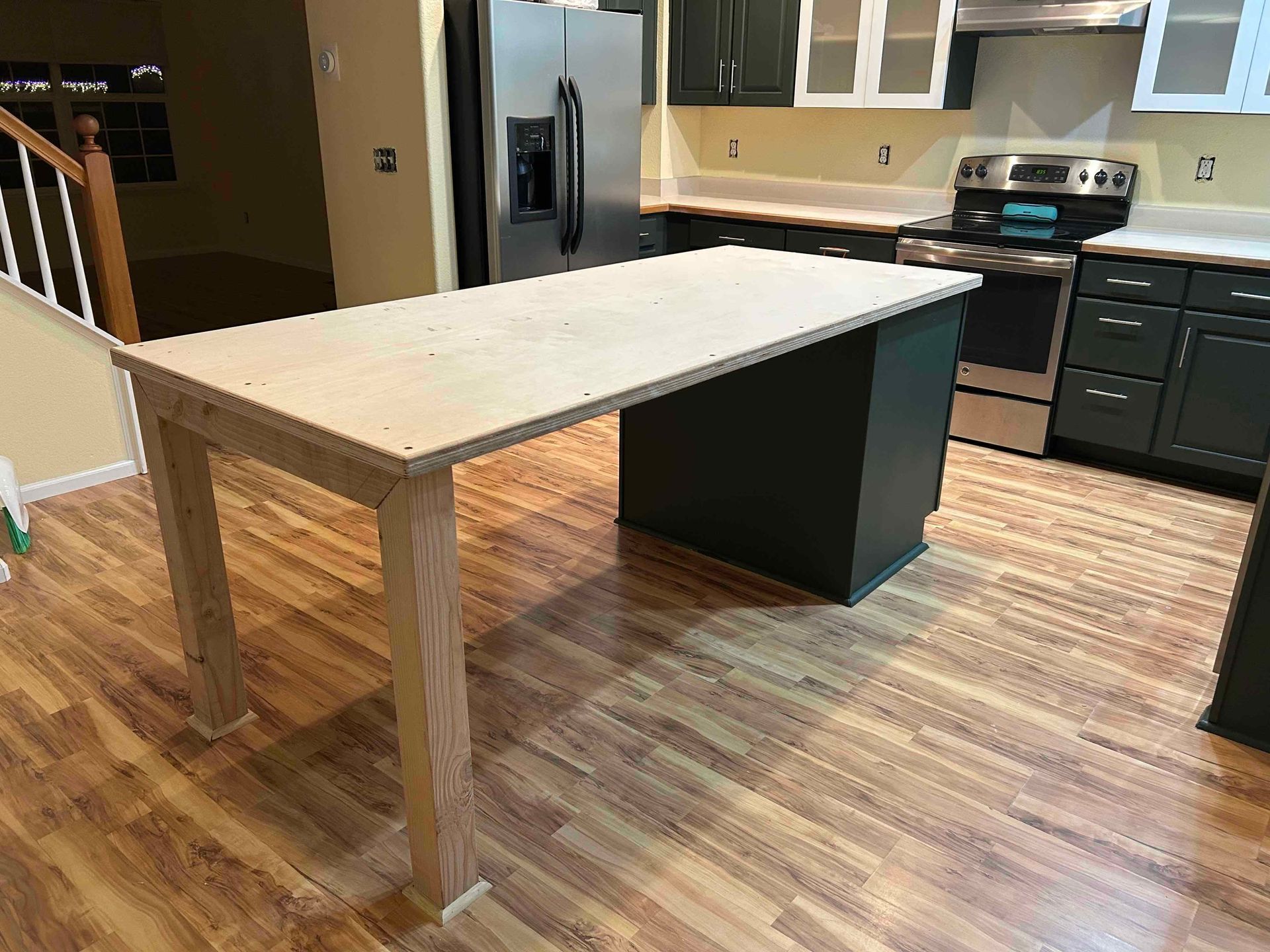 Kitchen with wood floor and dark green cabinets. Kitchen island with light wood legs, gray countertop.