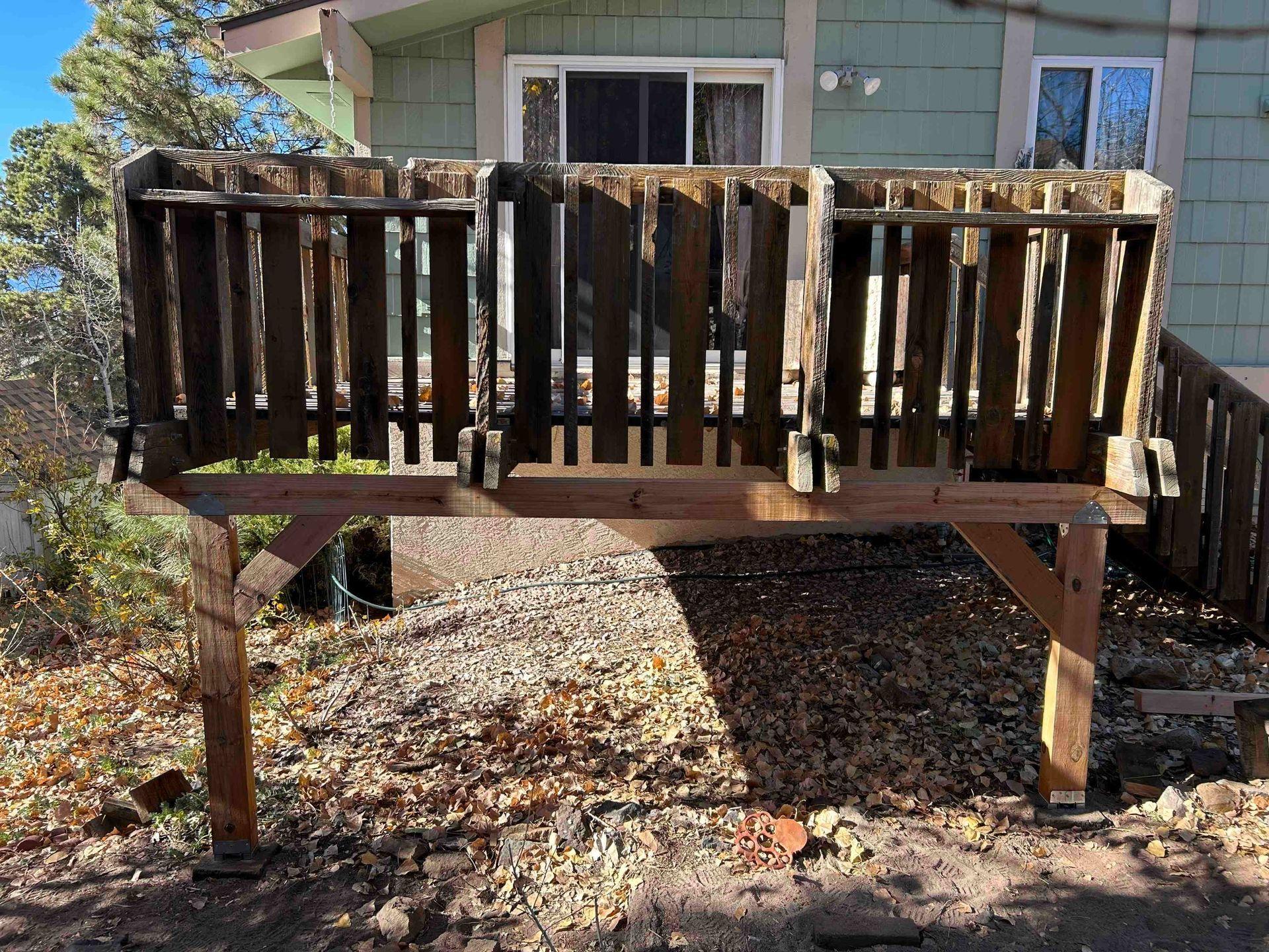 Wooden deck with weathered railing; gravel base; green building in background.