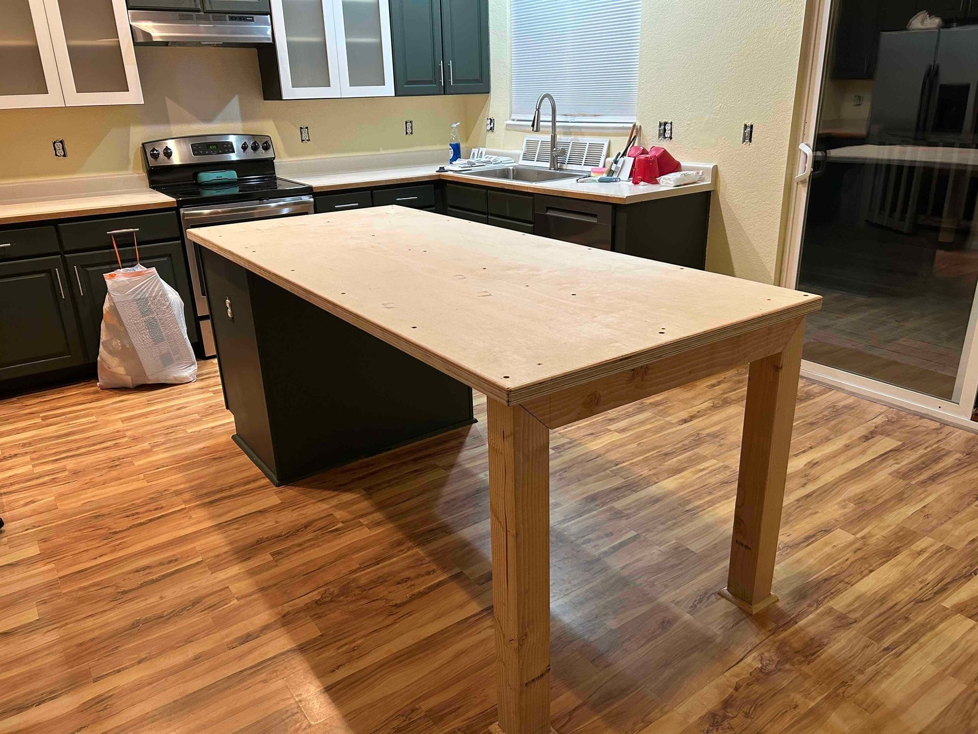 Kitchen with a wooden island in the center; dark cabinets, light countertops, and wooden flooring.