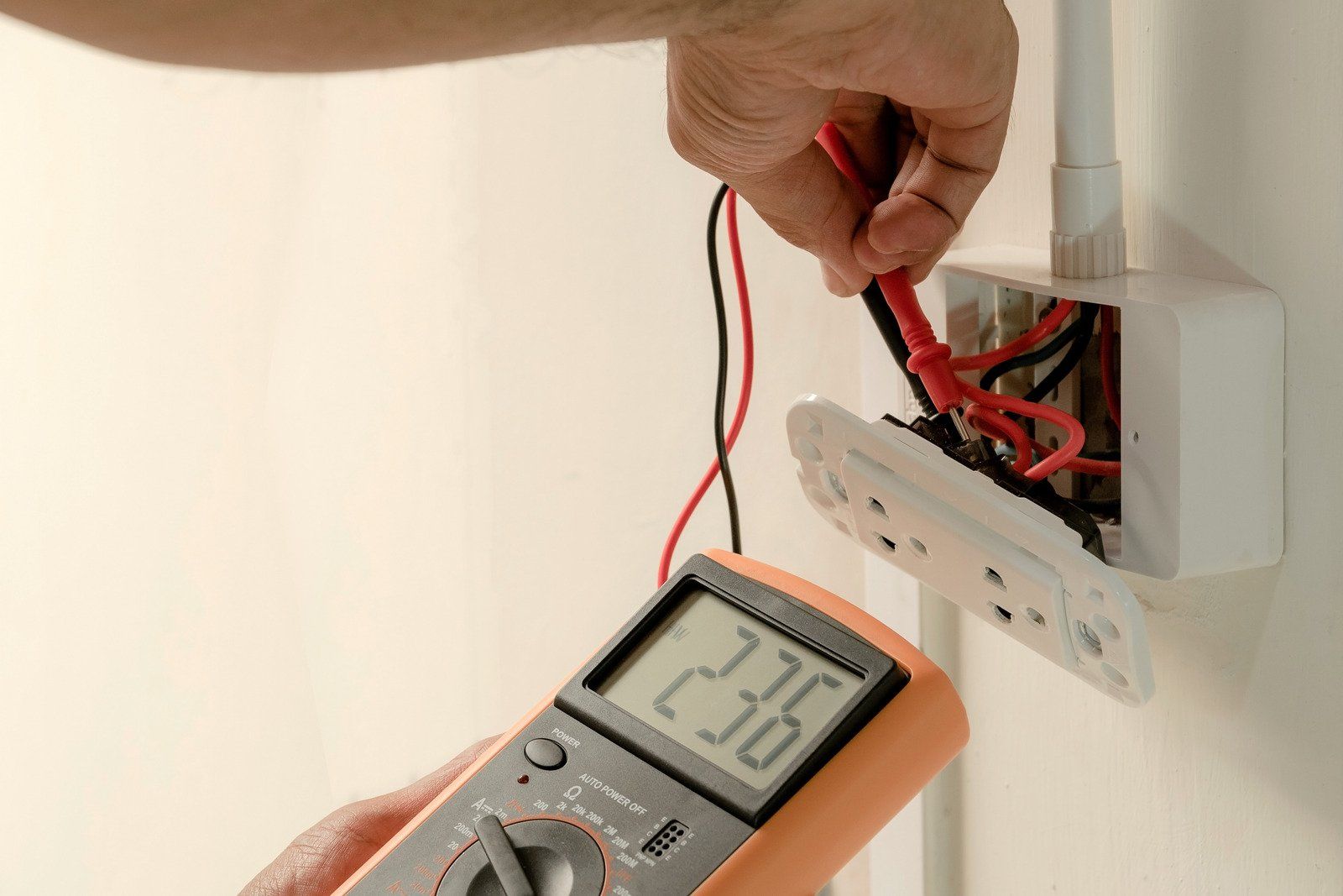 Electrician testing outlet voltage with a multimeter, reading 236, indoors.