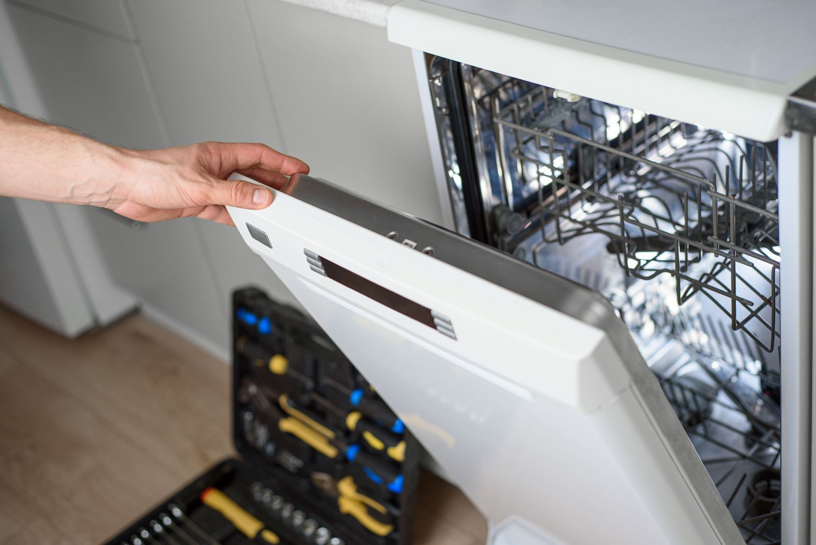 Repairman in blue cap and striped shirt testing a microwave with a multimeter in a kitchen.