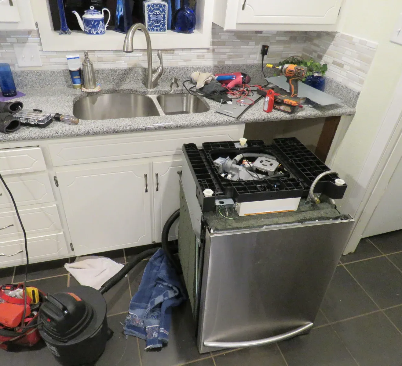 A repairman in blue overalls fixing a washing machine in a bathroom.