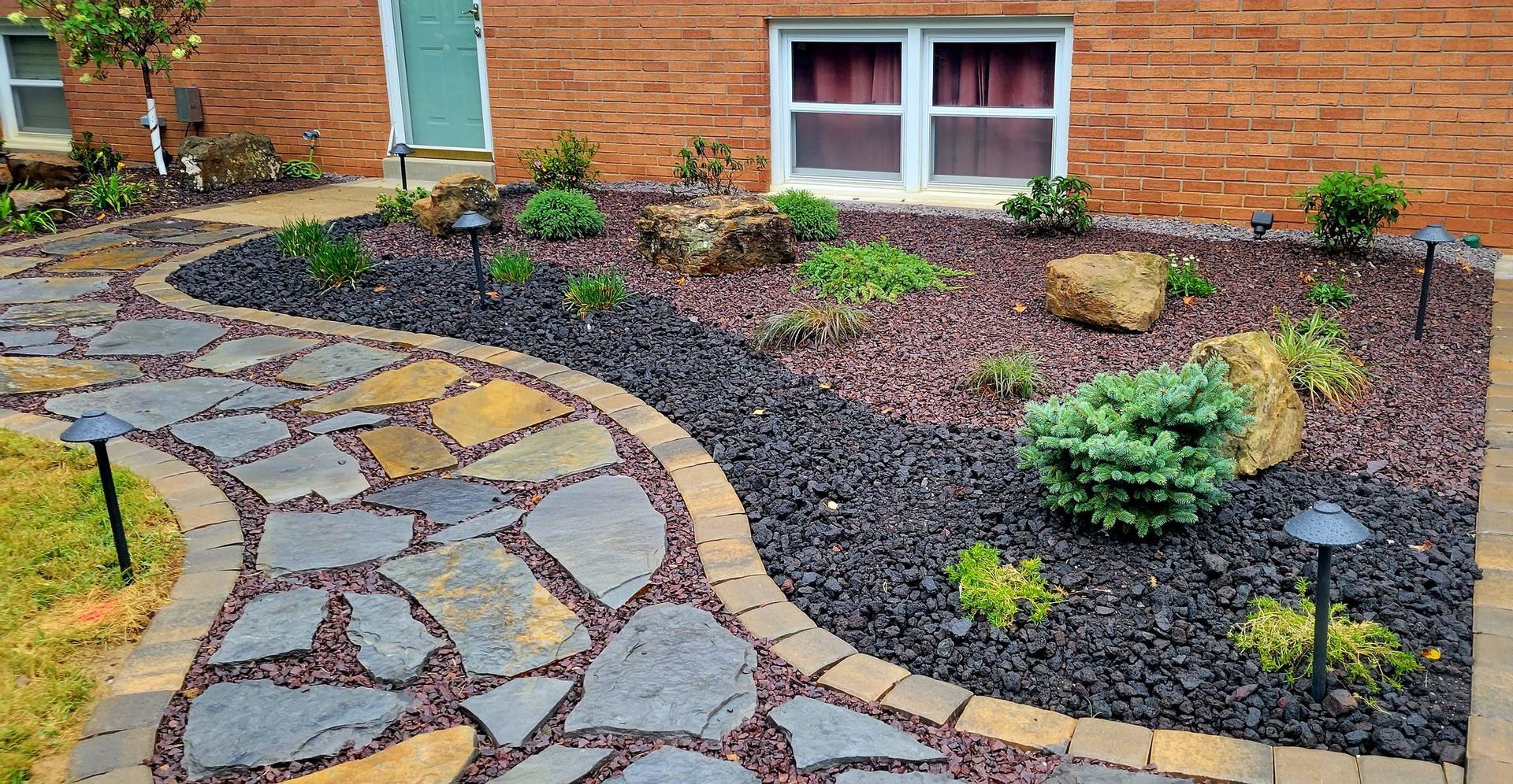 A stone walkway leading to a brick house with a garden in front of it.