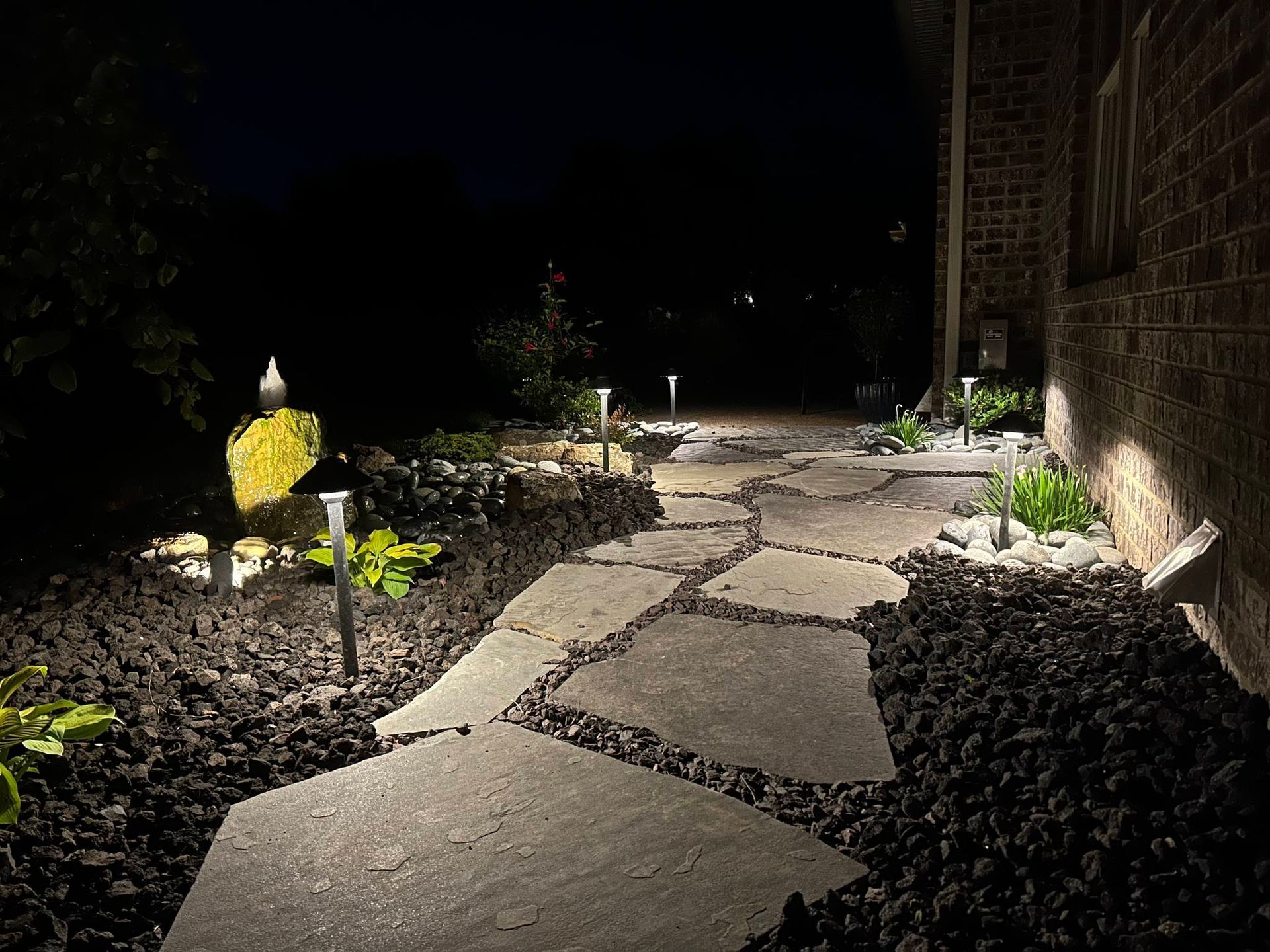 A stone walkway is lit up at night in front of a brick building.