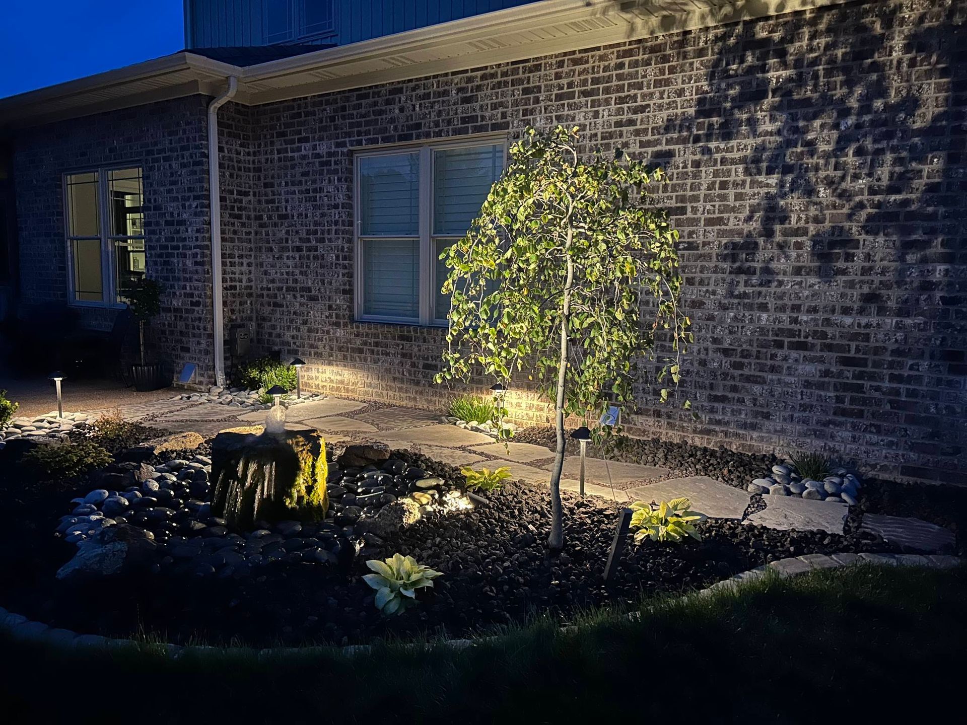 A brick house with a tree in front of it is lit up at night.