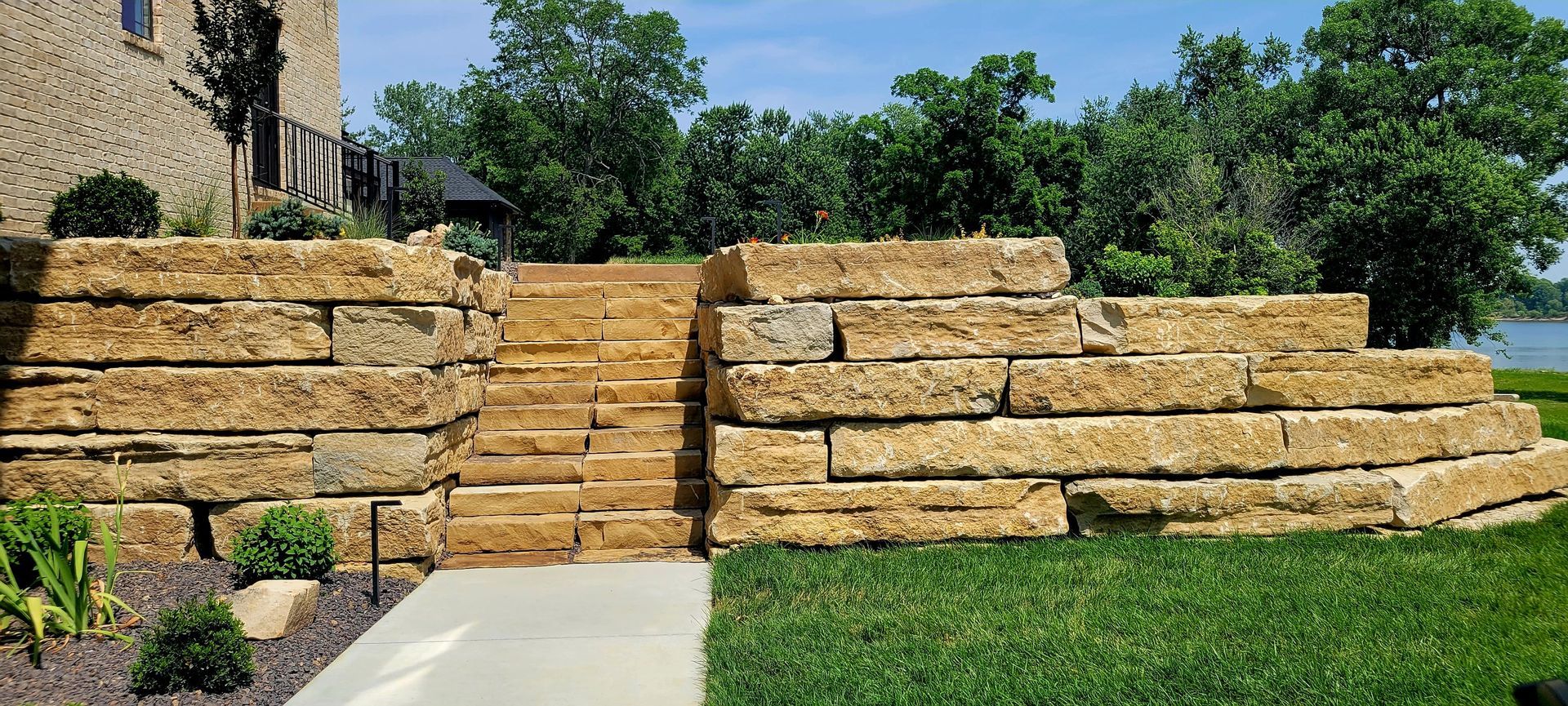 A large stone wall with stairs leading up to it in front of a house.