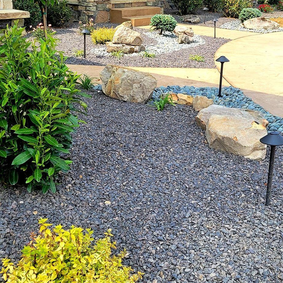 A garden with gravel , rocks , plants and lights.