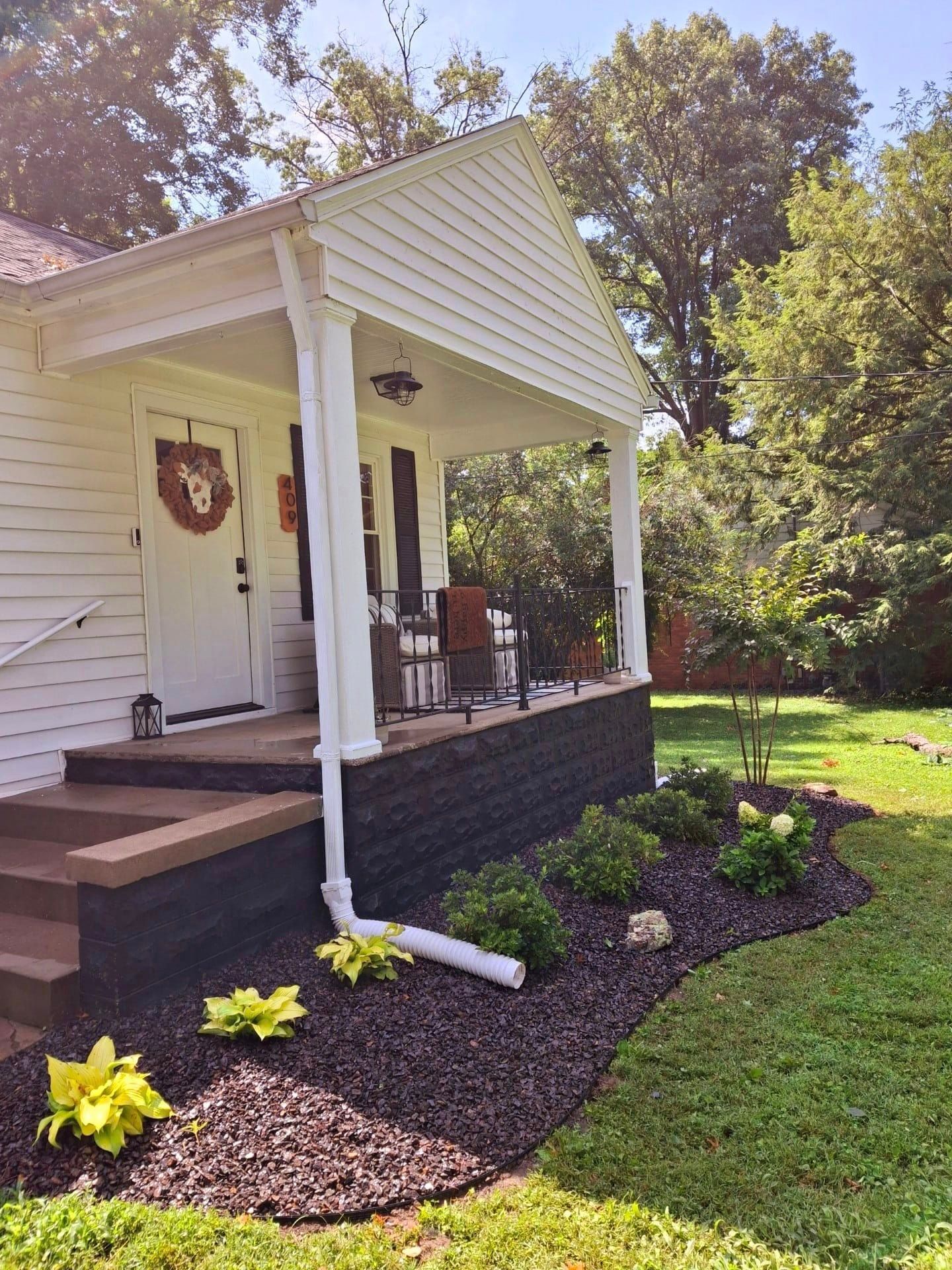 A white house with a porch and stairs in a lush green yard.