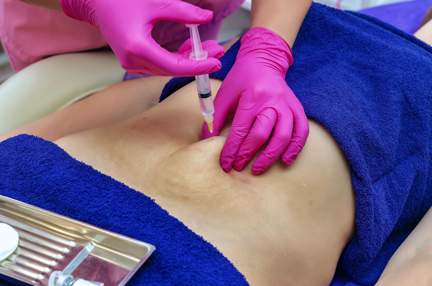 Person receiving an injection in the abdomen, administered by someone wearing pink gloves.