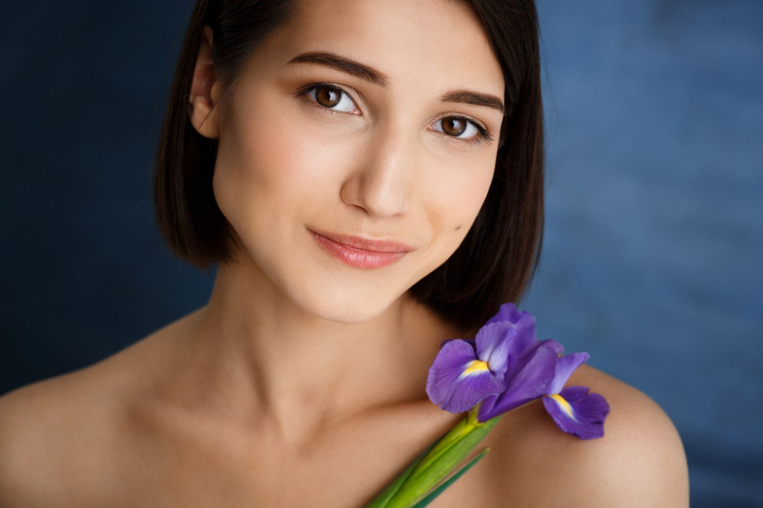 A woman is holding a purple flower on her shoulder.