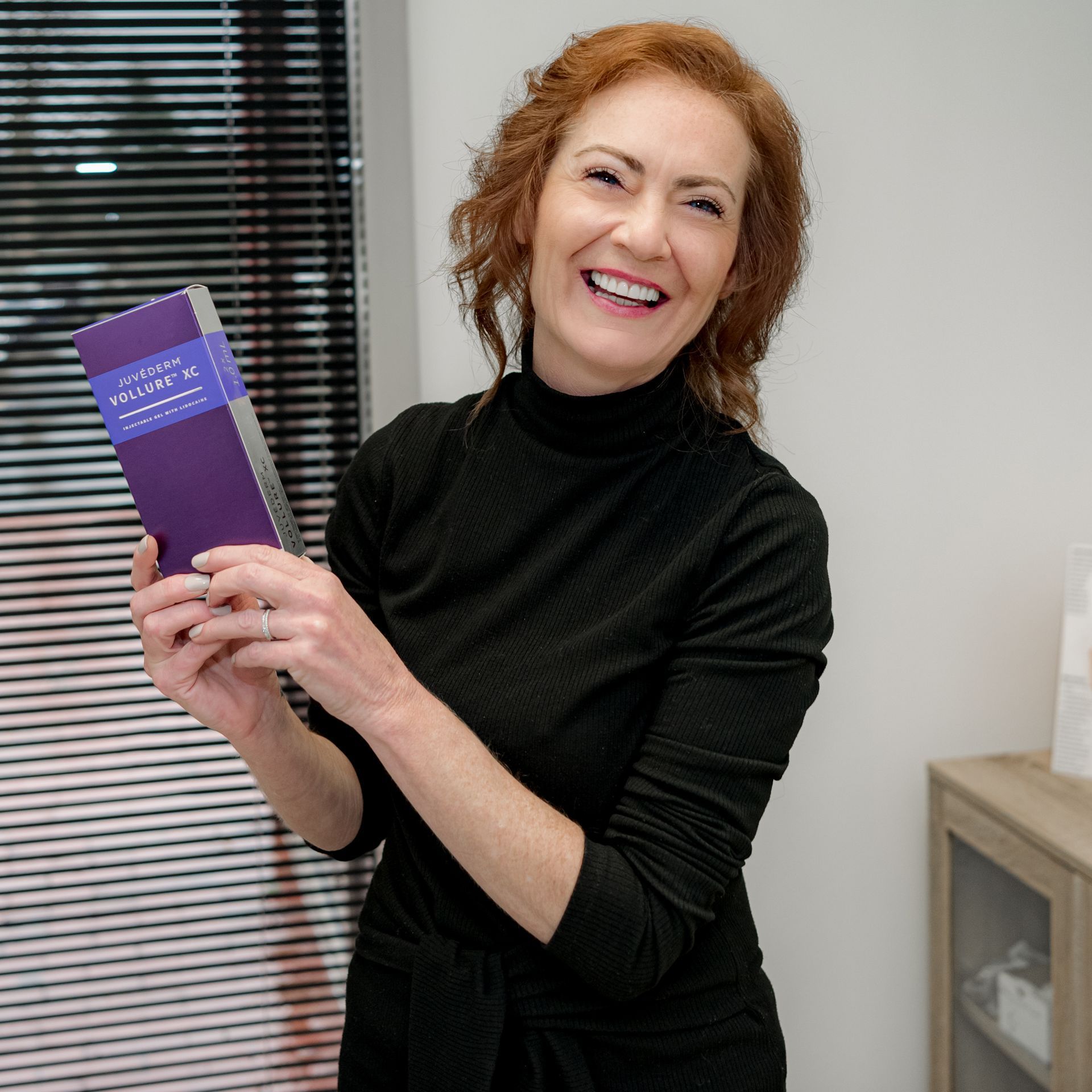 A woman in a black dress is holding a purple book and smiling