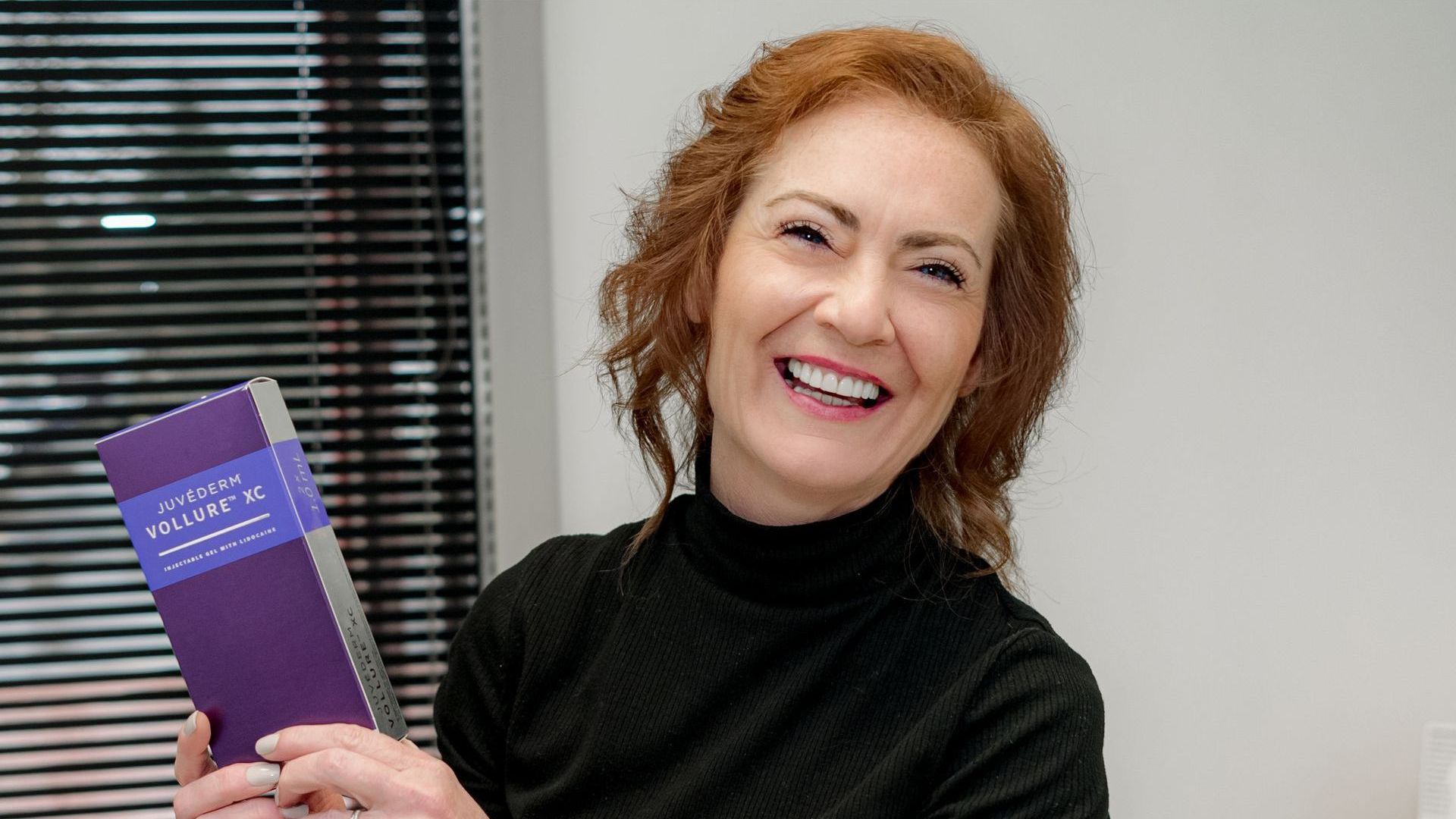 A woman in a black dress is holding a purple book and smiling