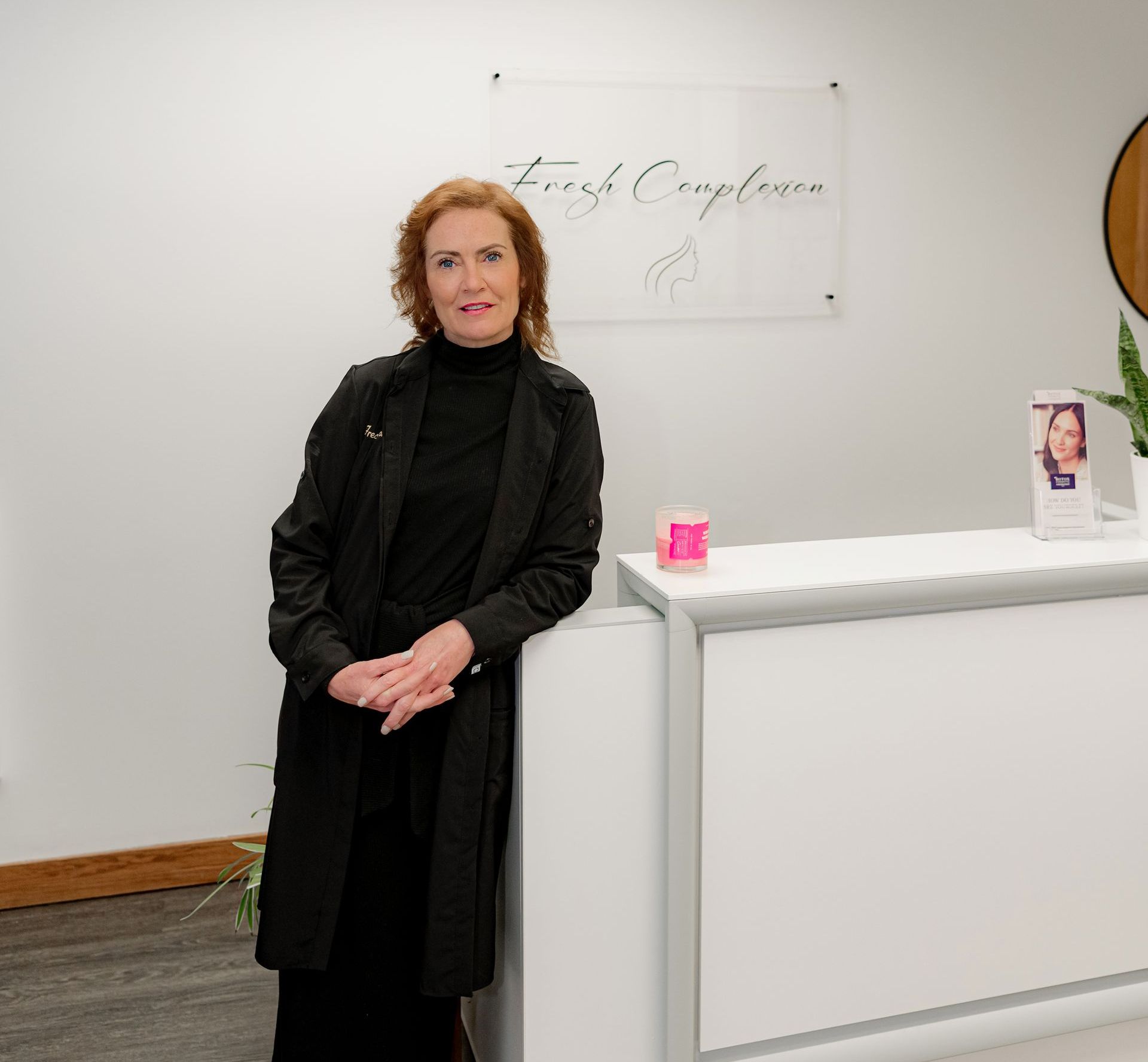 Woman in black outfit leans on white reception desk in a business. Sign reads