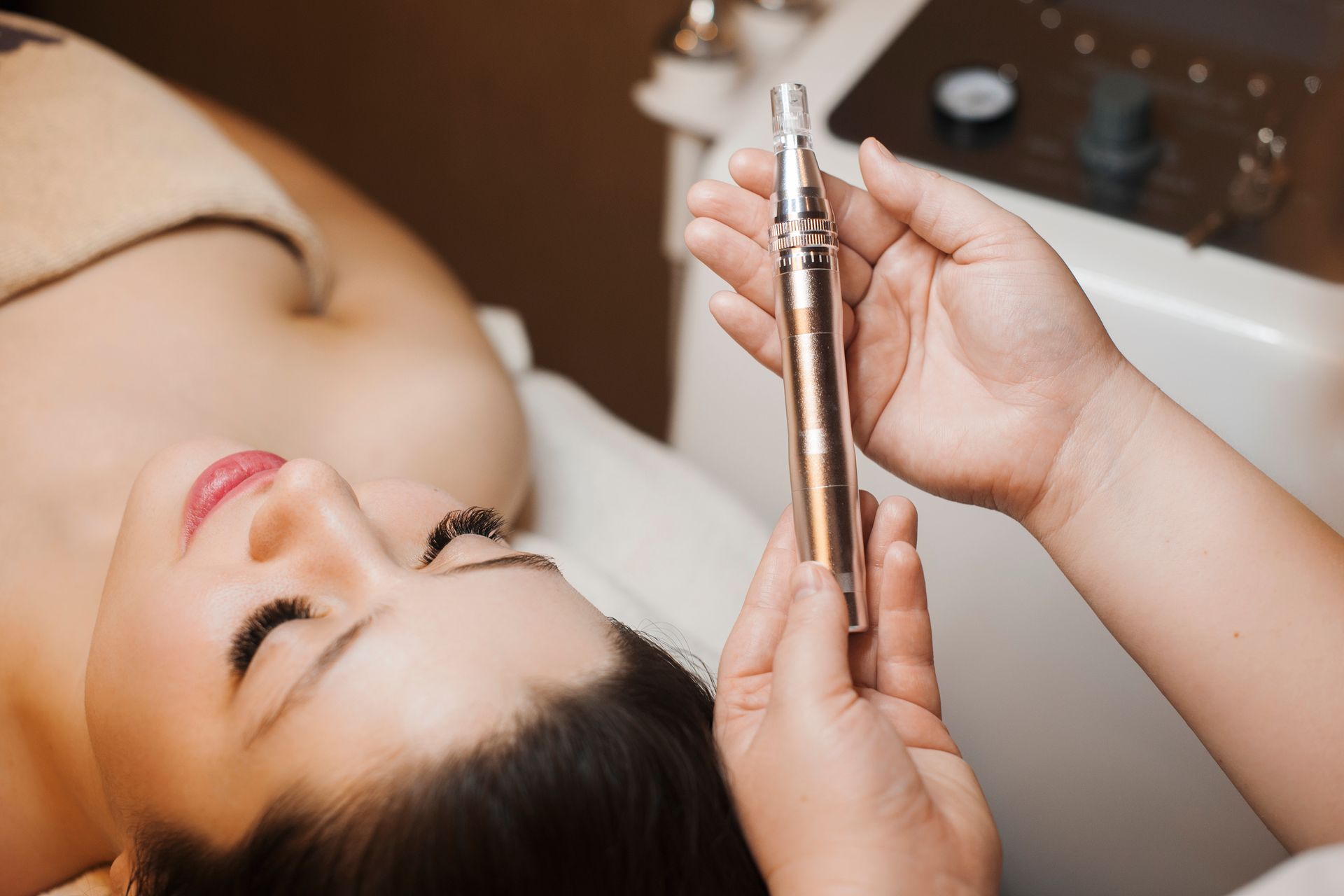 A practitioner holds a microneedling device near a person lying on a spa treatment table.