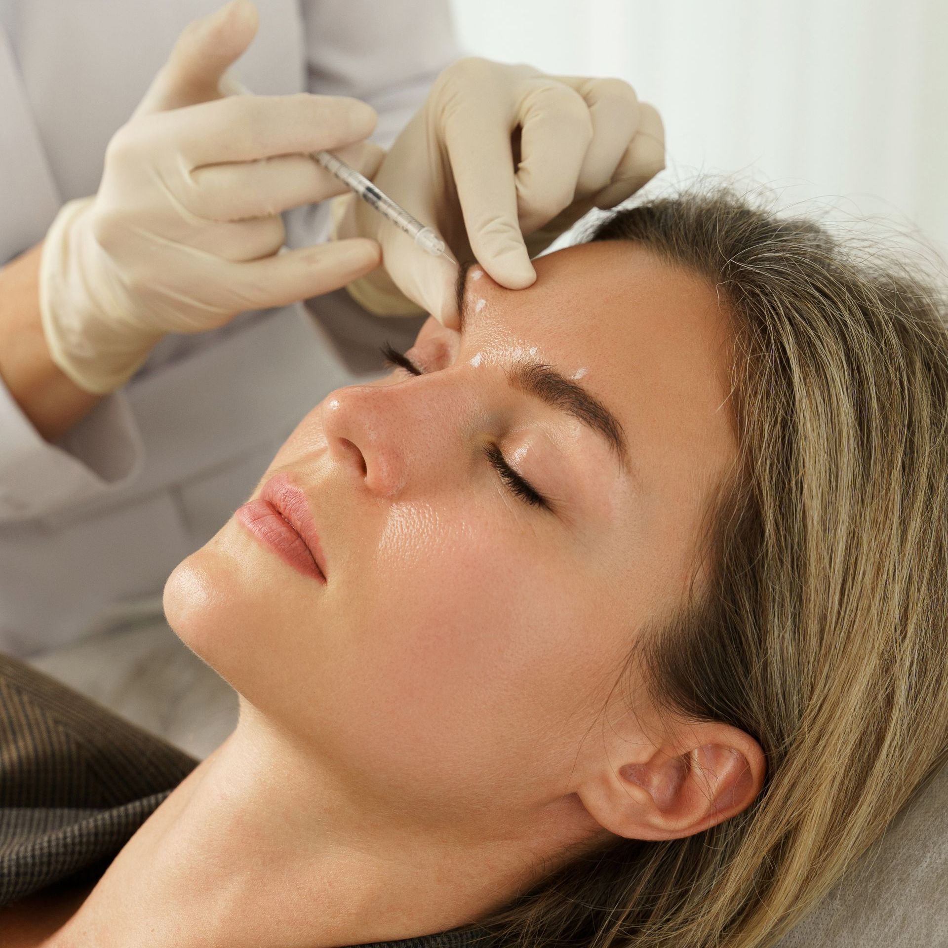 A woman is getting a botox injection on her forehead