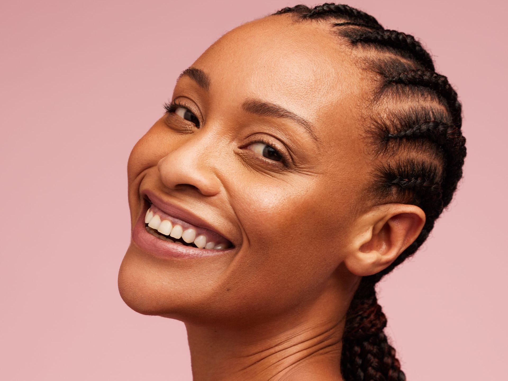 A woman with braids is smiling and looking over her shoulder.