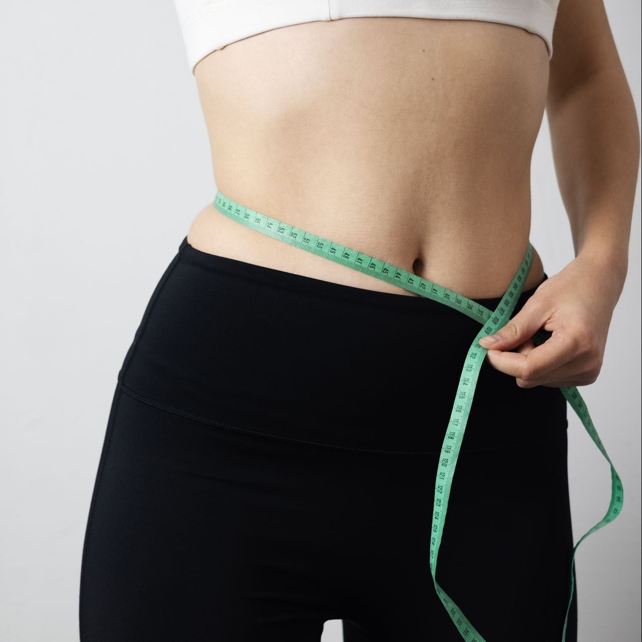 A woman is measuring her waist with a tape measure.