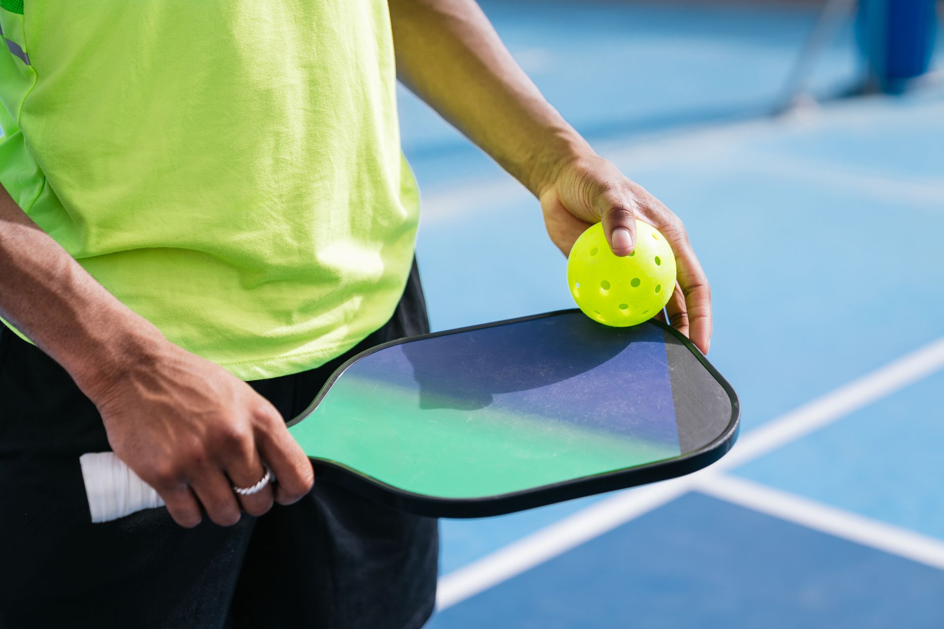A person is holding a paddle and a tennis ball on a tennis court.