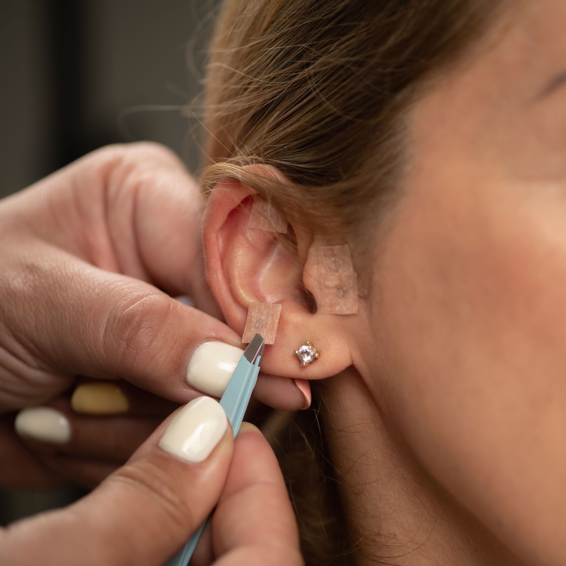 A woman is getting her ears pierced with a pair of earrings.
