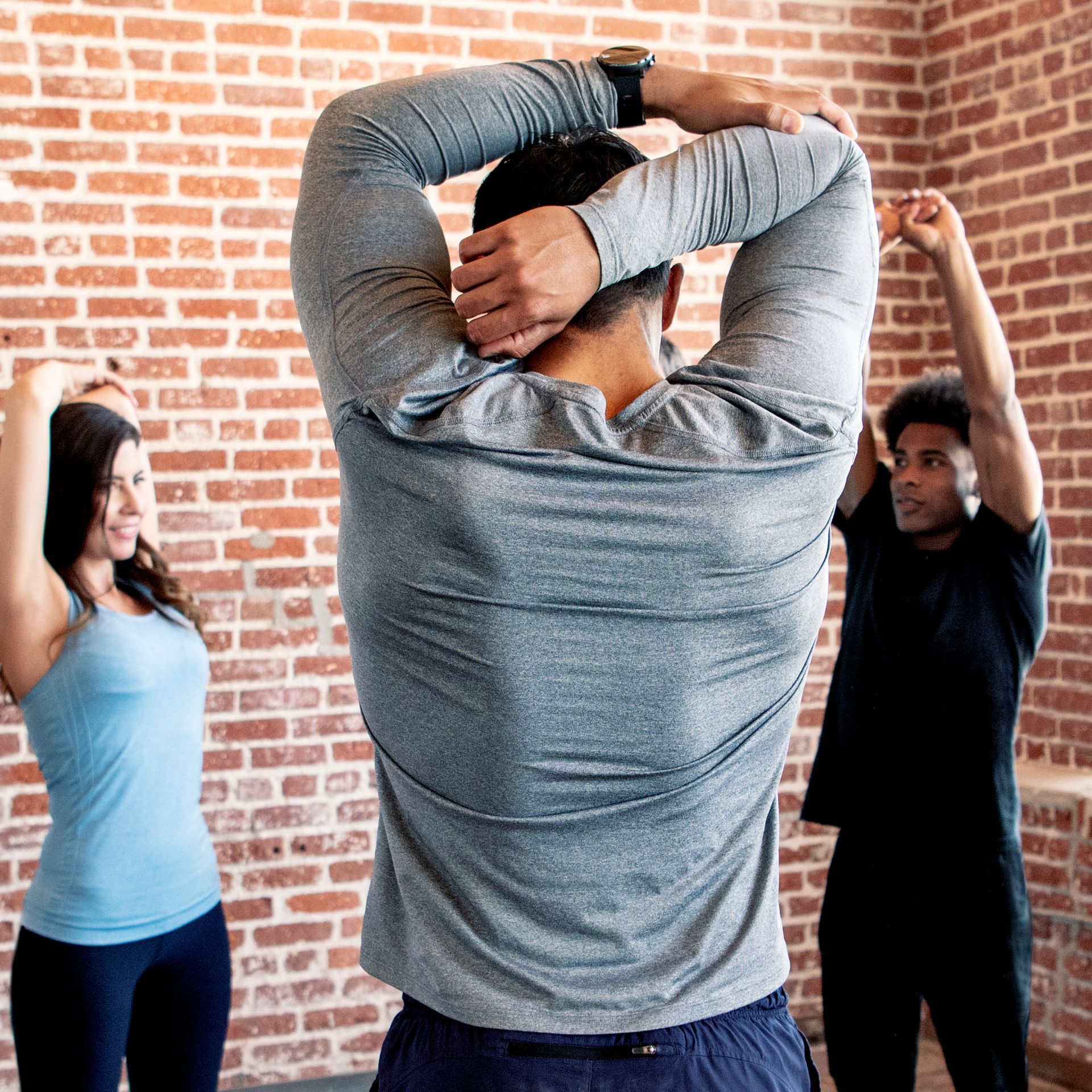 A group of people are stretching their arms in front of a brick wall.