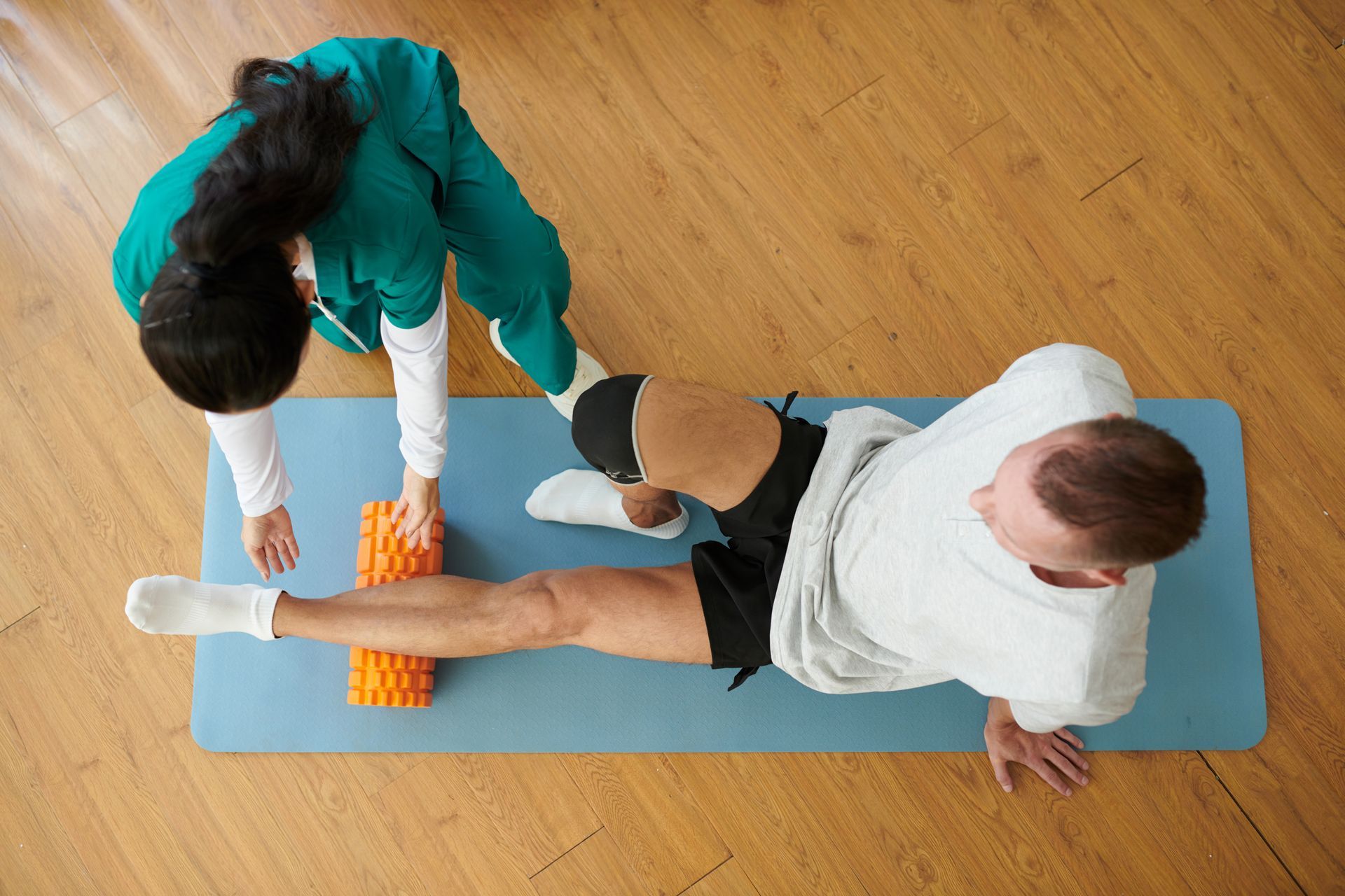 A woman is helping a man stretch his leg on a yoga mat.