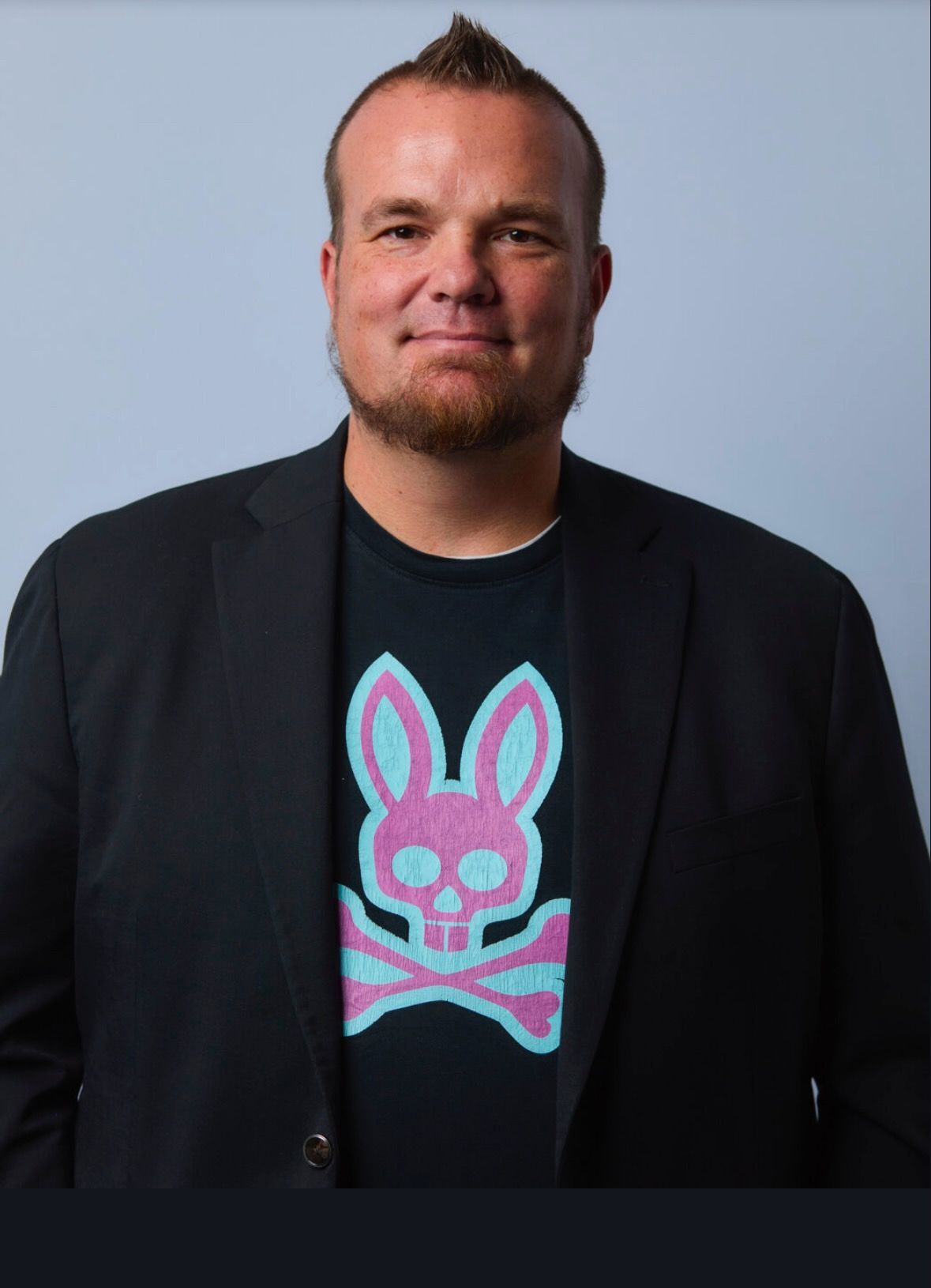 A man with a beard and glasses is smiling with his arms crossed.