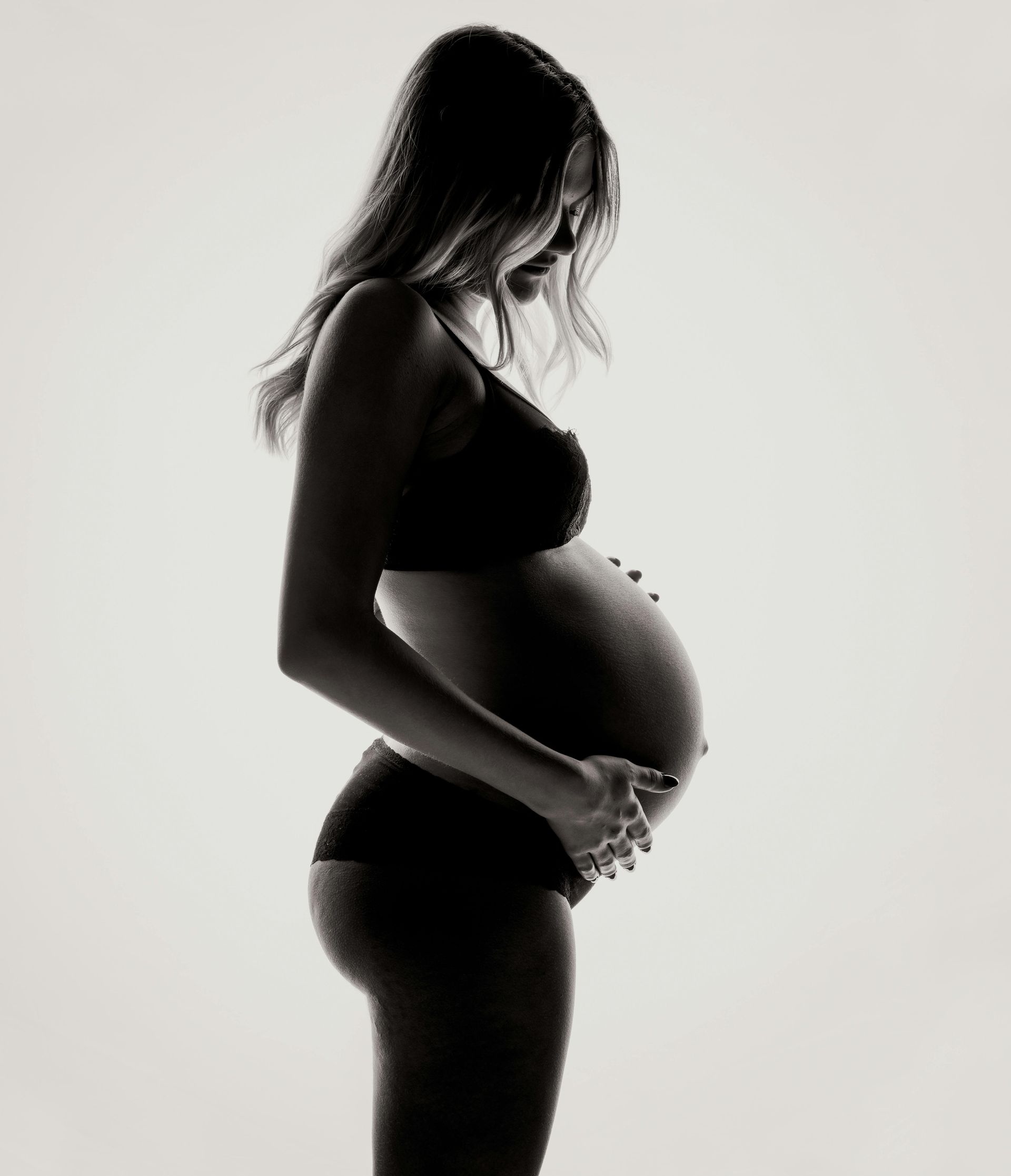 A black and white photo of a pregnant woman holding her belly.