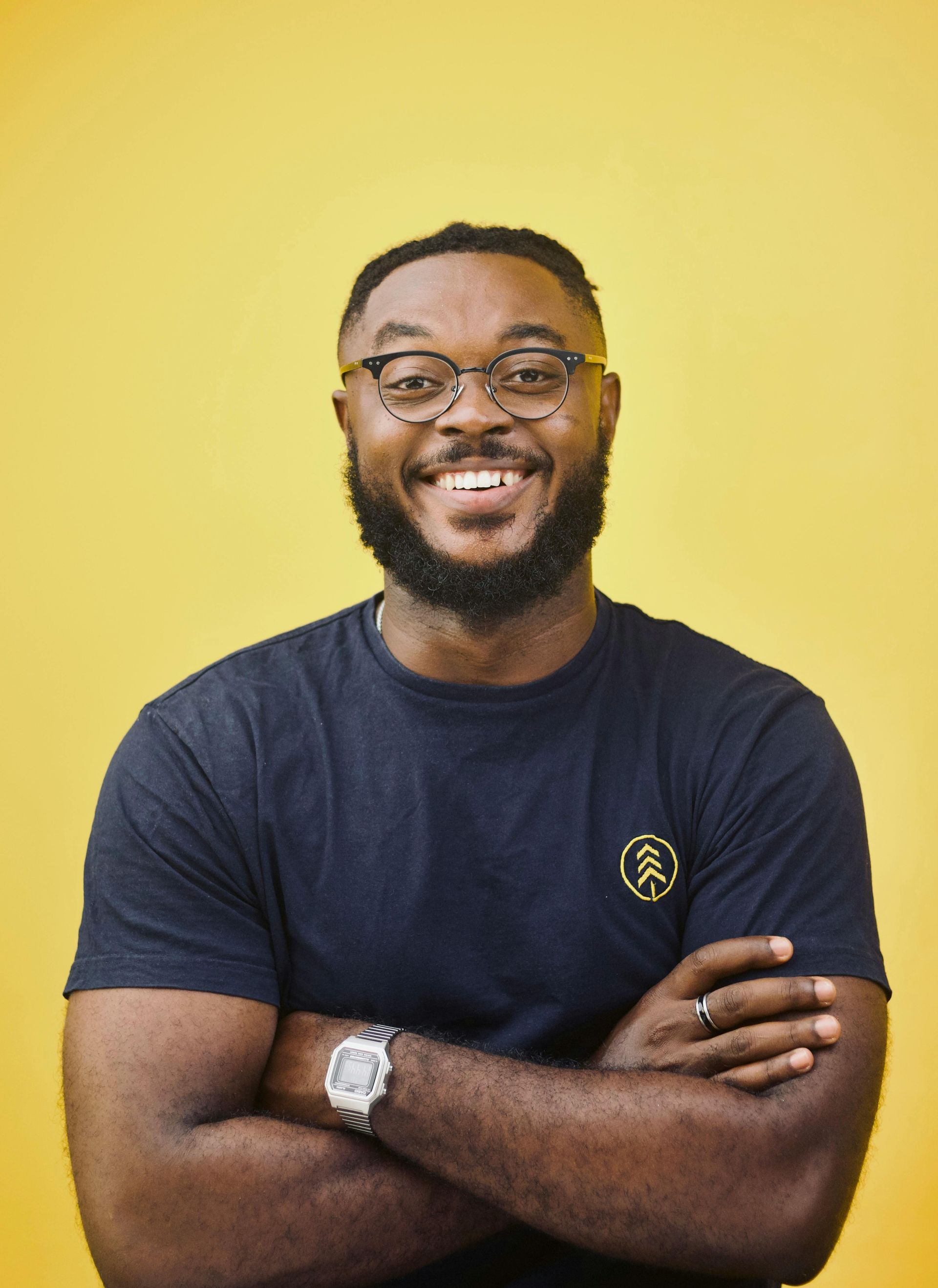 A man with a beard and glasses is smiling with his arms crossed.