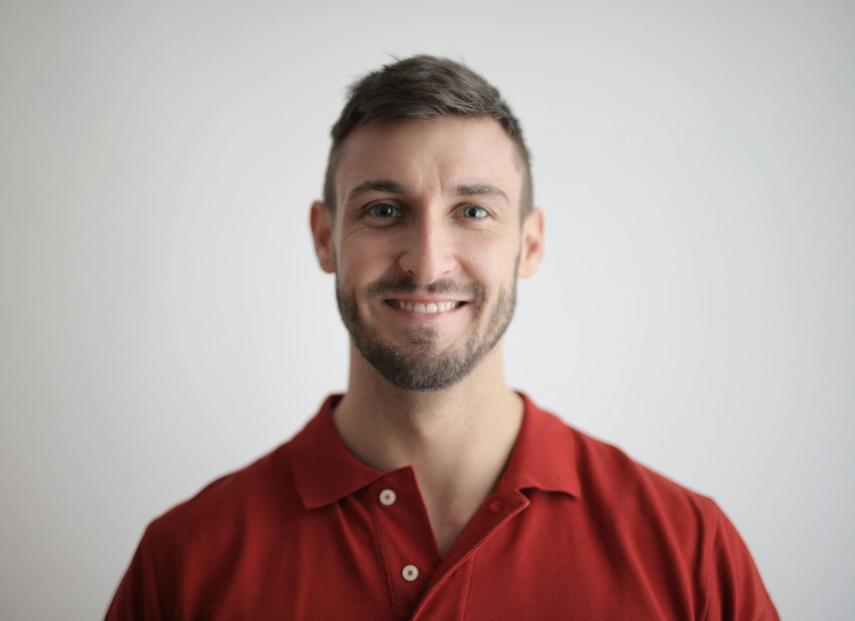 A man with a beard is wearing a red polo shirt and smiling.