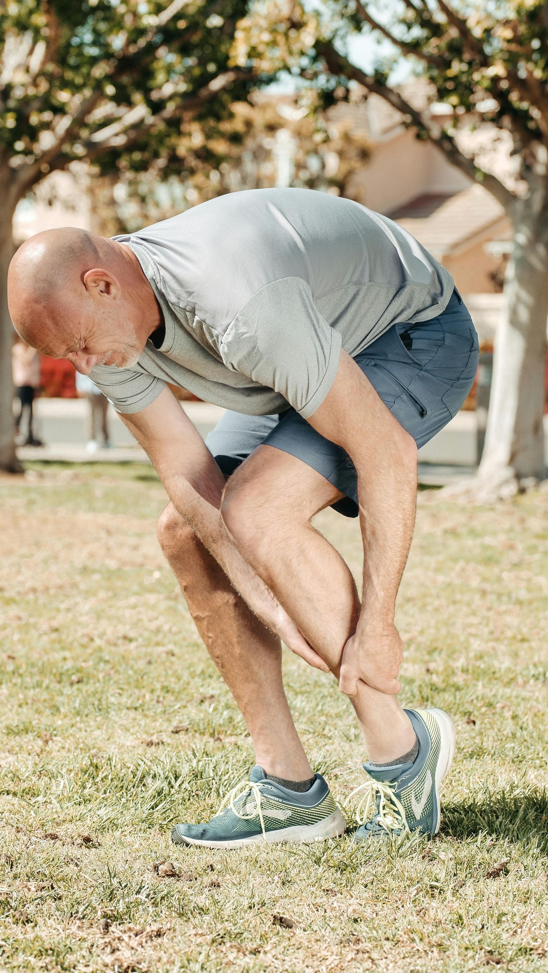 A man is kneeling down in the grass holding his ankle in pain.