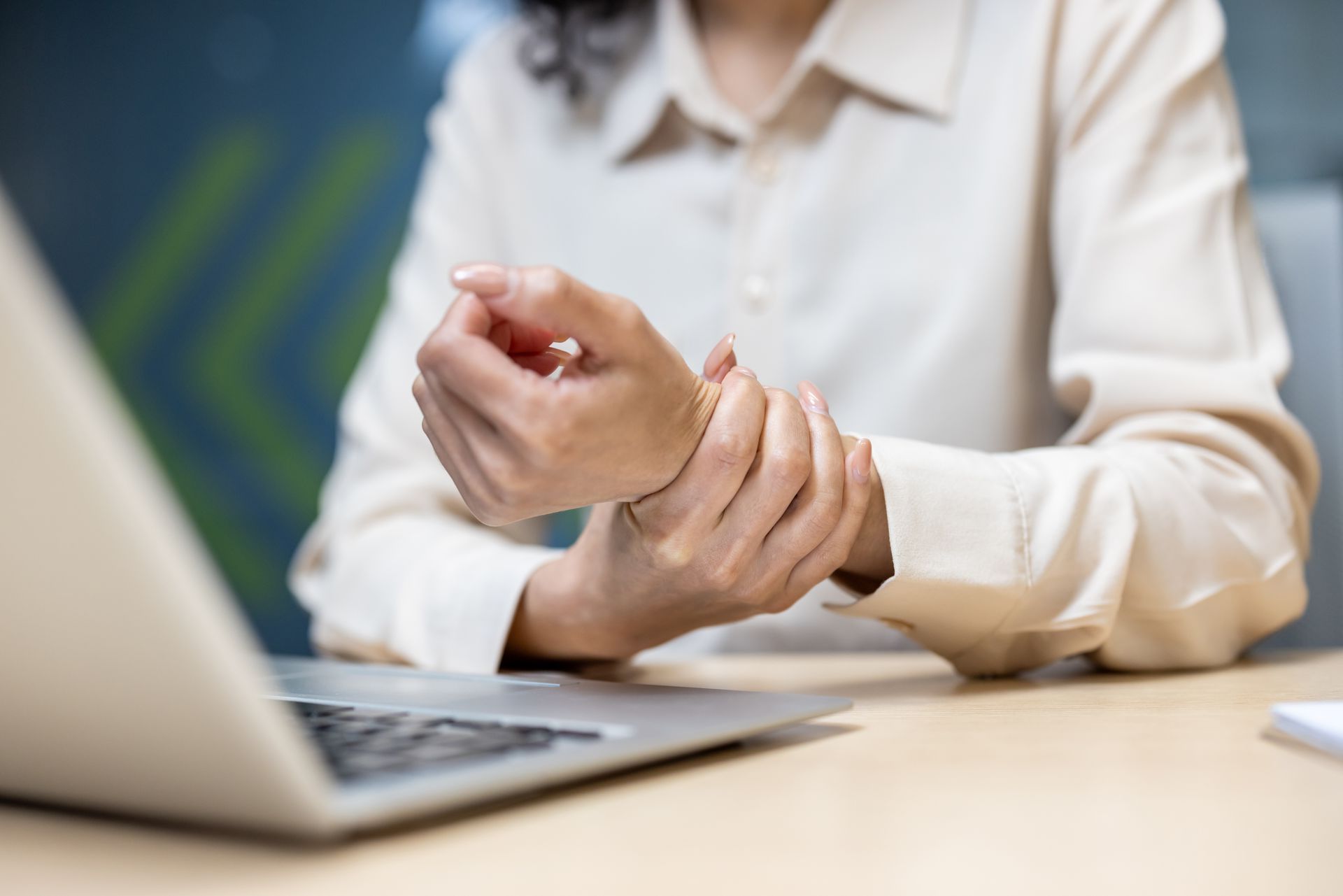 A woman is sitting at a desk holding her wrist in pain.