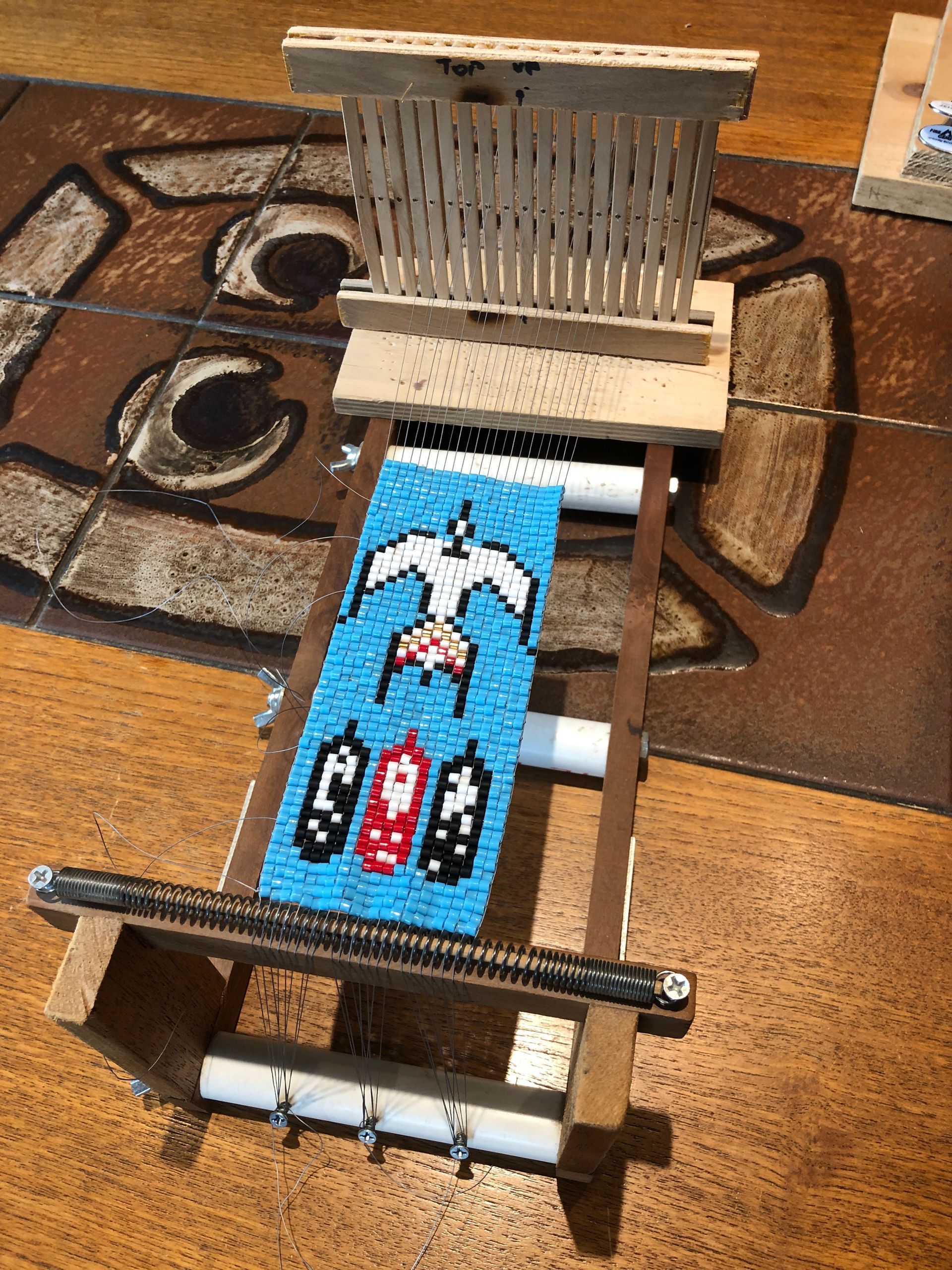 Beaded loom with a blue and white eagle design, and red and black feathers.