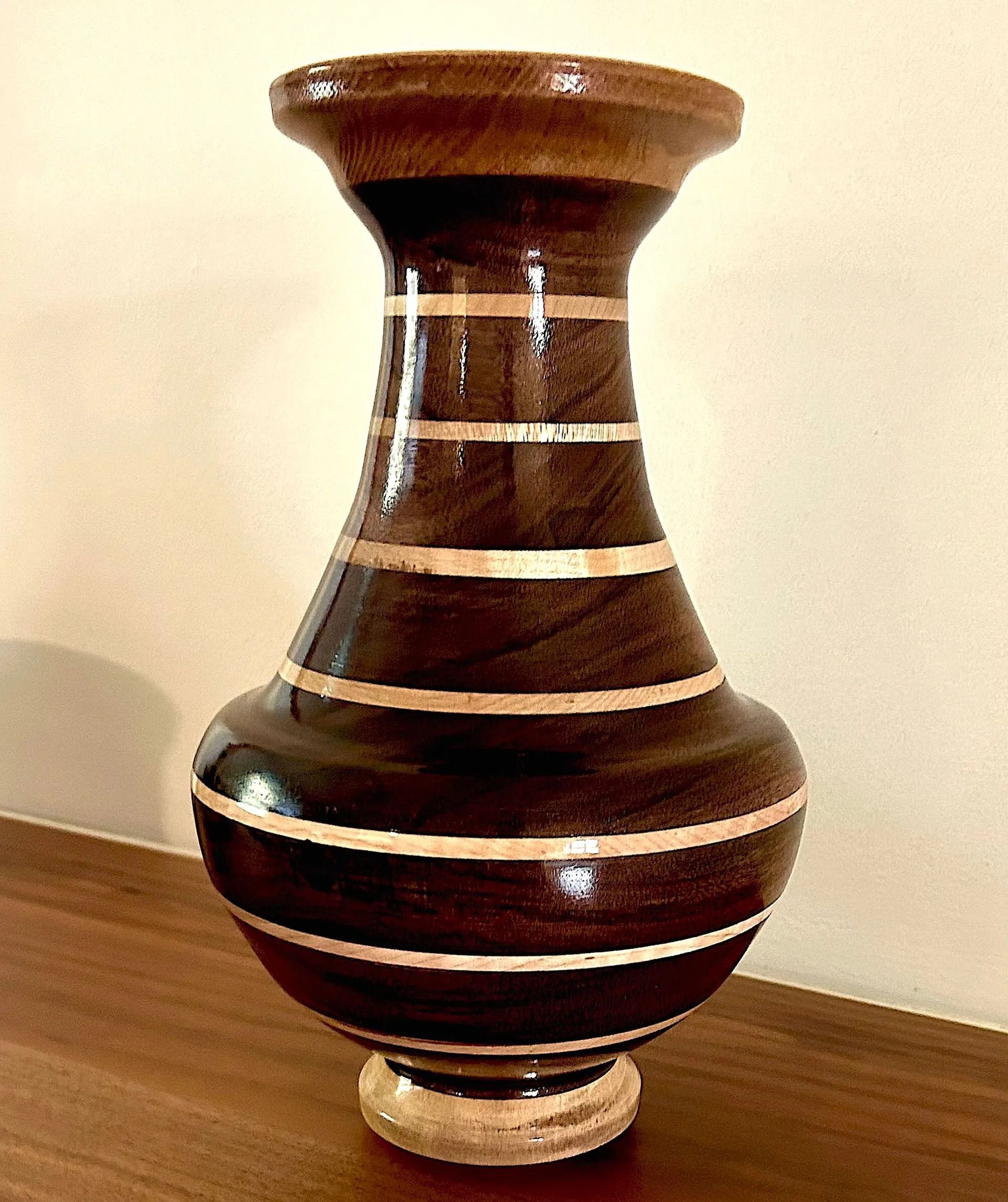 Wooden vase with dark brown body, light stripes, and base, sitting on a wooden surface.