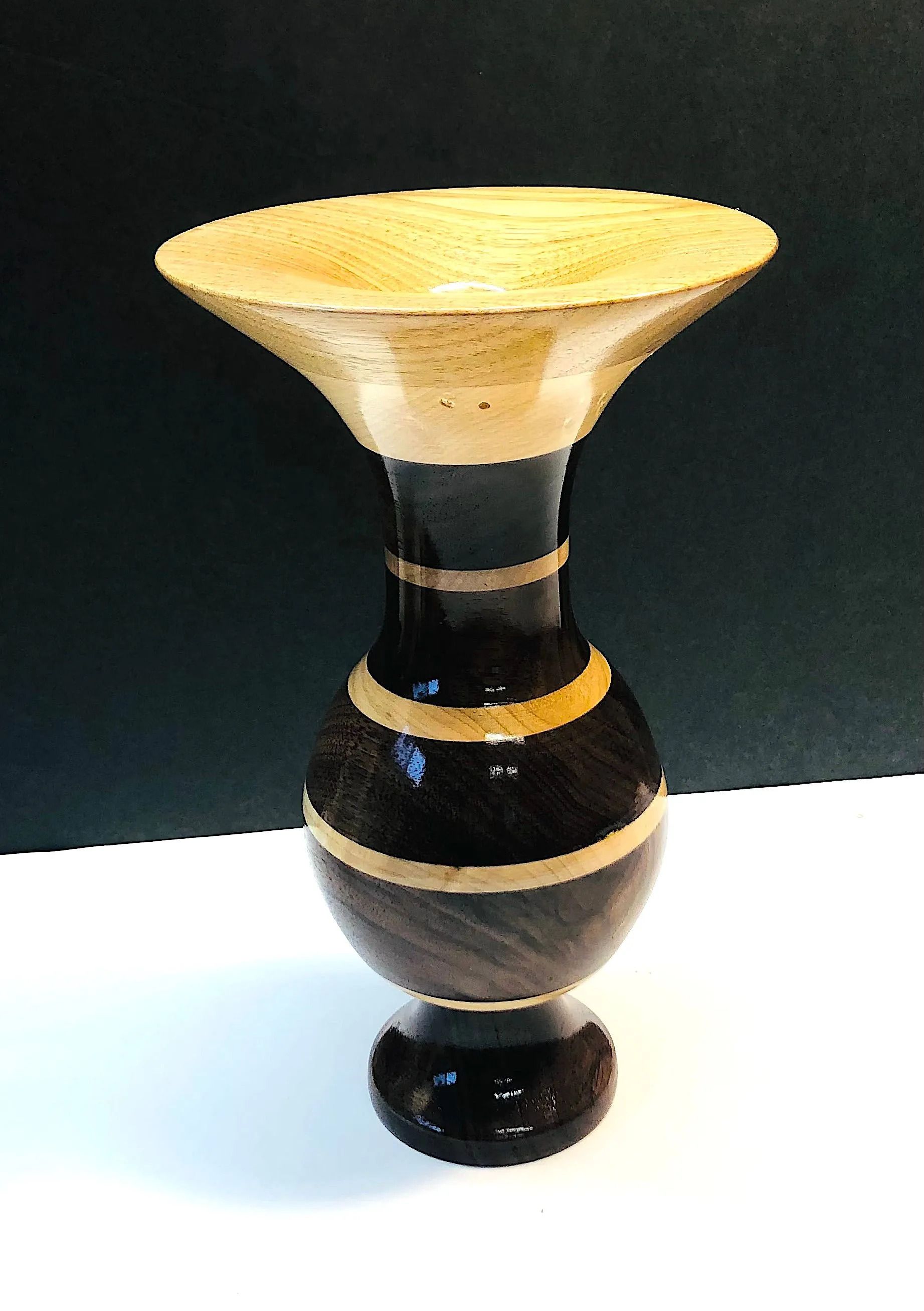 Wooden vase with black and tan sections, flared top, spherical body, and rounded base.