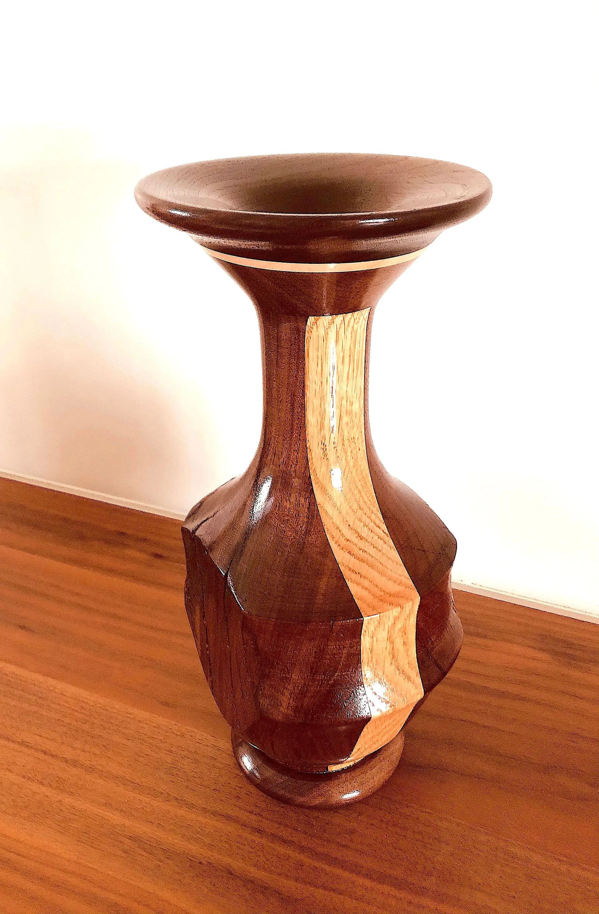 Wooden vase, dark brown with a light-colored wood stripe, on a wooden surface.