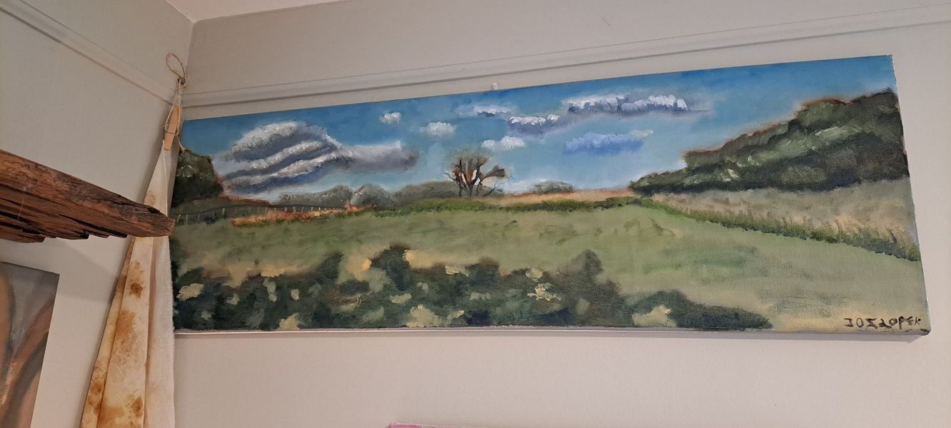 Landscape painting on a wall; green fields, blue sky with clouds.