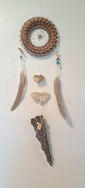 Dream catcher with feathers, stones, and driftwood on a white wall.