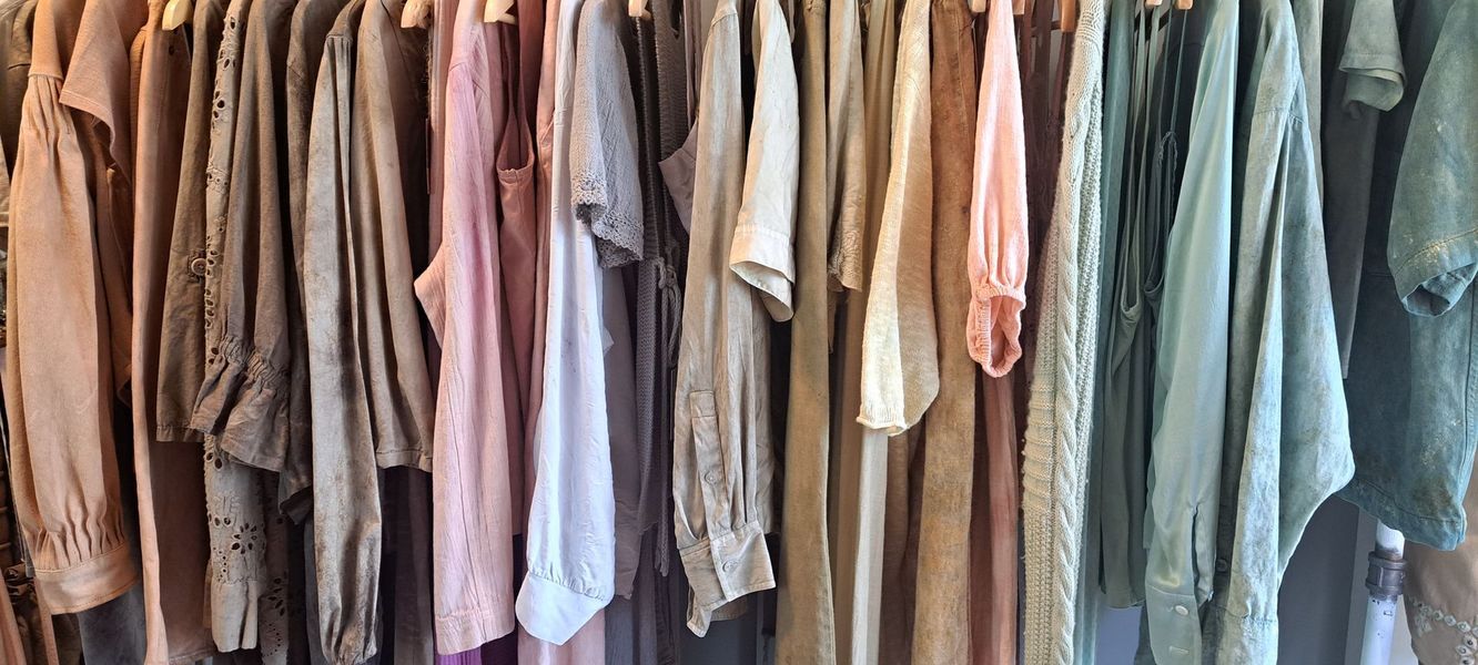 Clothes hanging on a wooden rack, mostly earth tones and pastels.