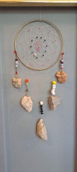 Dream catcher with beads and stones hanging against a gray wall.