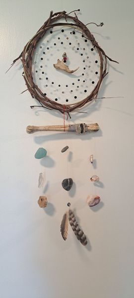 Dreamcatcher hanging on a white wall. It has a woven twig ring with beads and charms dangling below.