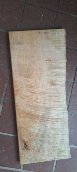 A light-brown rectangular wooden board lies on a brown tiled floor. The wood grain is visible.