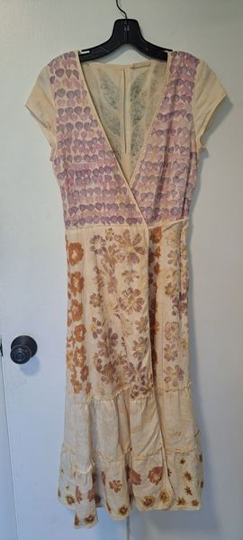 Cream-colored dress with floral and purple pattern, hanging on a black hanger against a white door.
