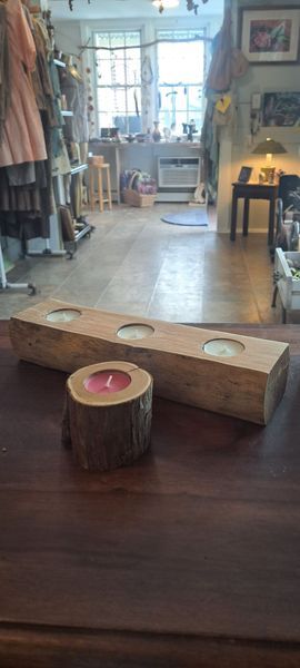 Wooden candle holders on a dark brown surface in a room. One log candle holder, one rectangular with three candles.