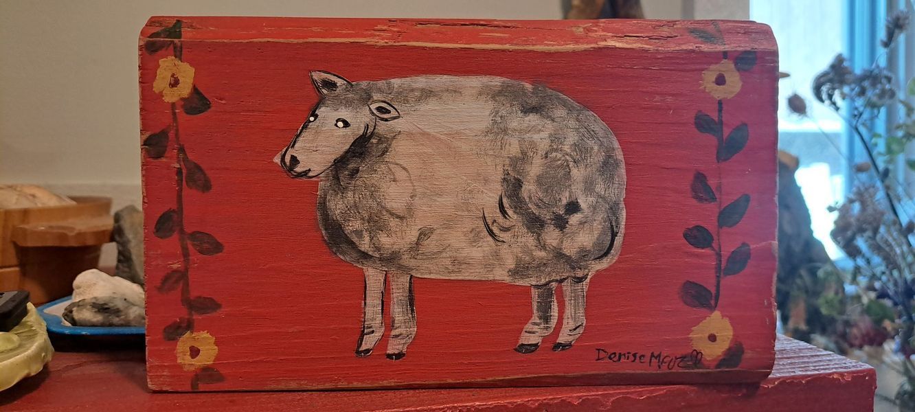 Red wooden box with painting of a sheep, surrounded by flowers and vines.