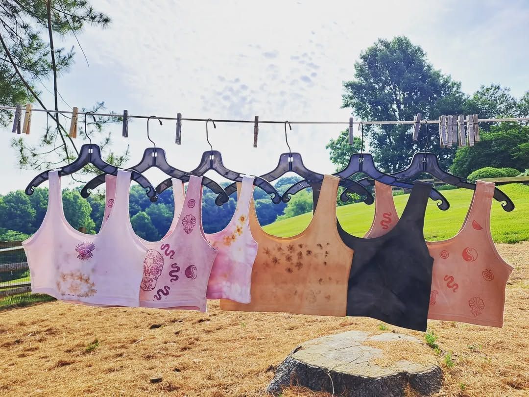 Clothes hanging on a clothesline outdoors: tank tops in various colors, with trees and sky in the background.