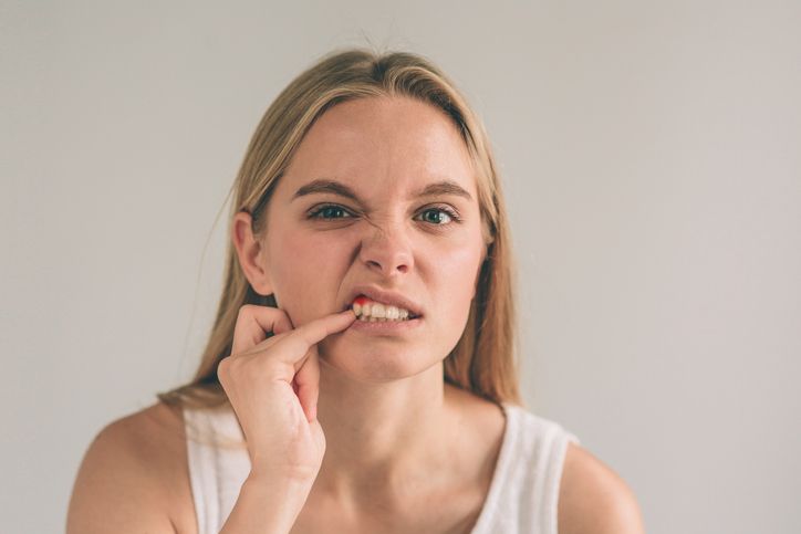 Woman touches her lip, grimacing while pointing at her teeth.
