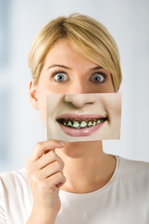 Woman holding a photo of teeth, covering her mouth; she has surprised expression.