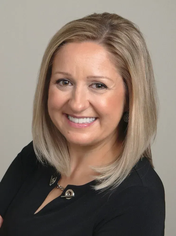 Woman with blonde hair smiling, wearing a black top against a gray backdrop.