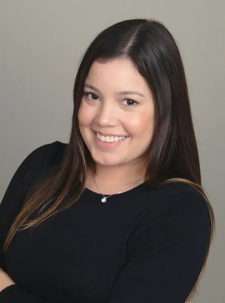 Woman with long, brown hair smiles at the camera, arms crossed, wearing a black top.